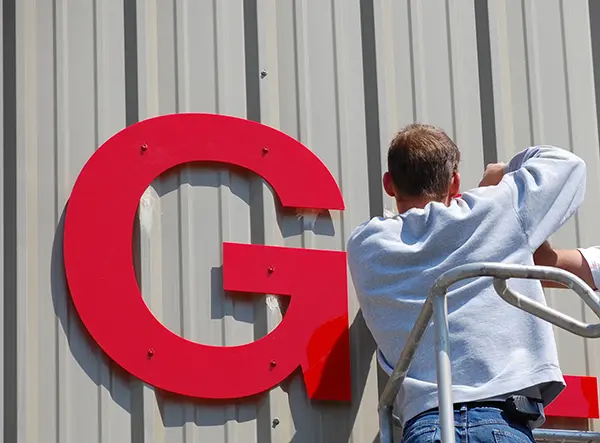 Man installing red G sign on side of building