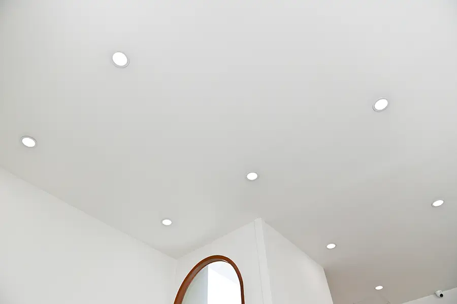 Round recessed lights on the ceiling with an arced wooden mirror